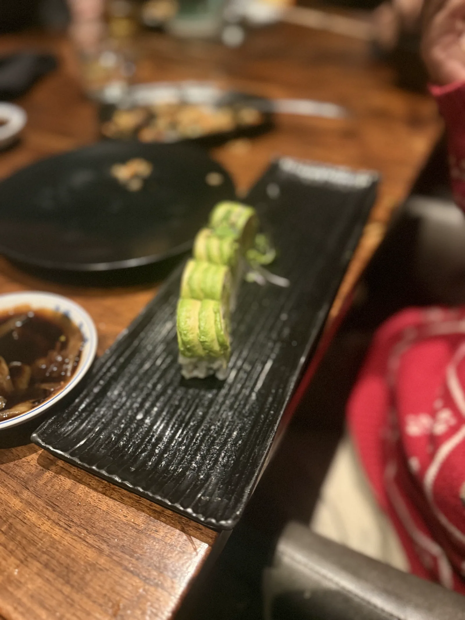 An avocado-wrapped sushi roll on a long black plate at Azabu