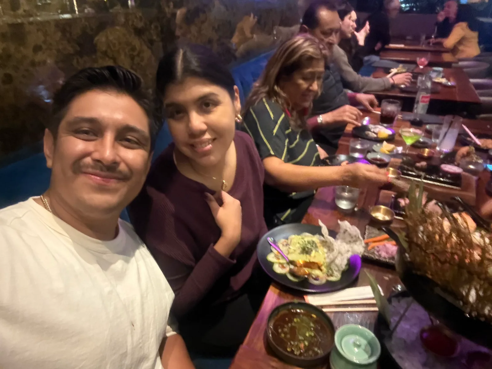 Family members smiling for a selfie at the long table at Azabu, with plates of food in front of them