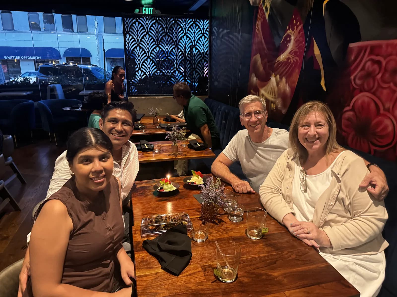 Family and in-laws smiling at a table at Azabu, with a colorful mural on one side and windows onto Philadelphia Street on the other