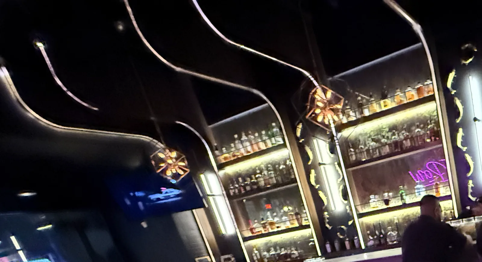 Azabu's back bar, with glowing shelves of bottles, curved gold light lines and copper star lanterns