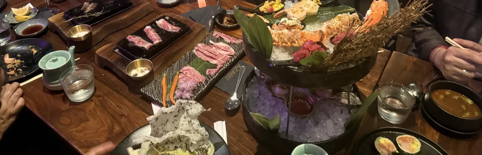 A long table at Azabu covered with the Premium Seafood Tower, plates of raw Wagyu, edamame and rolls