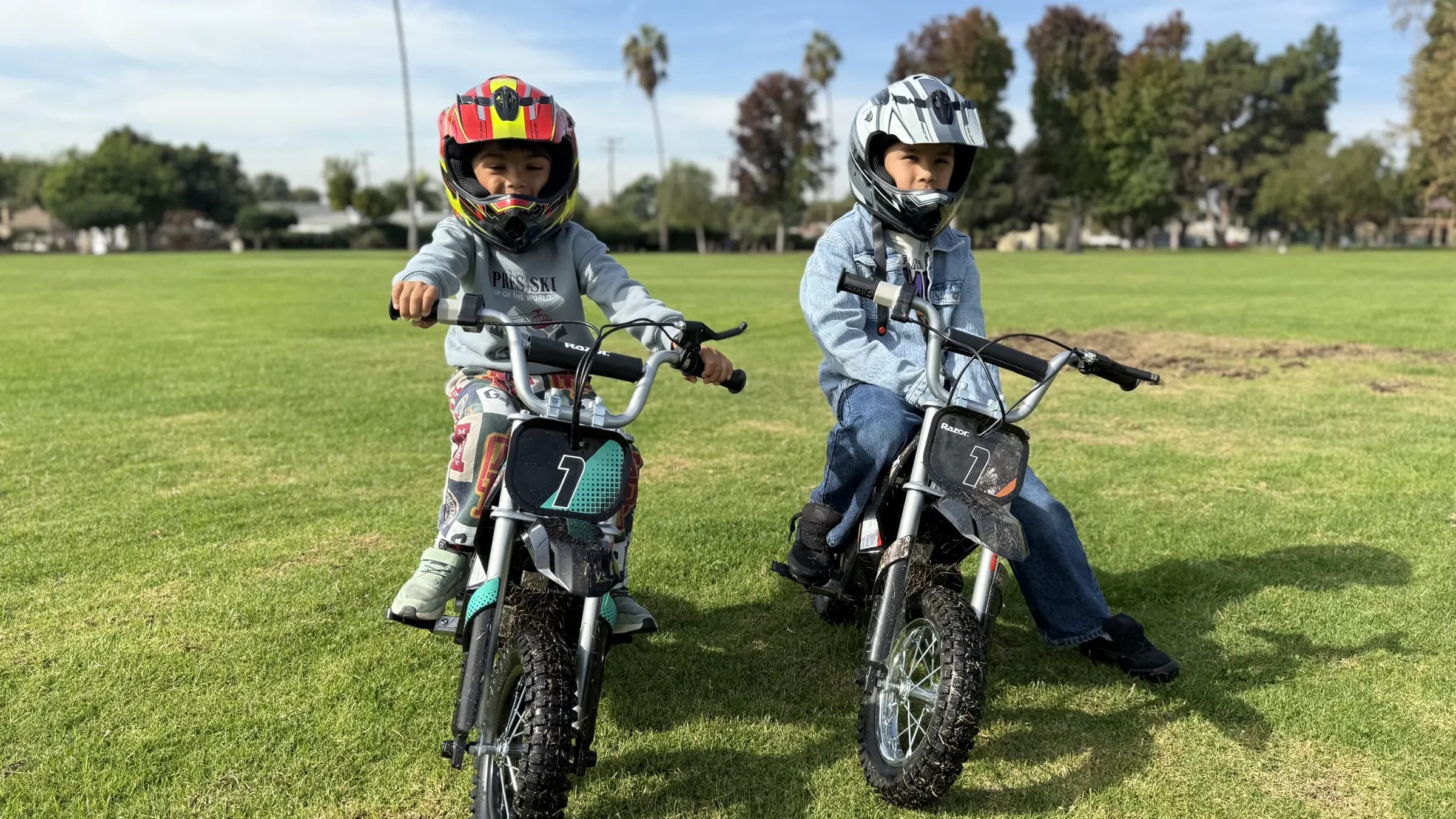 Dos niños con casco en motos pequeñas en un parque