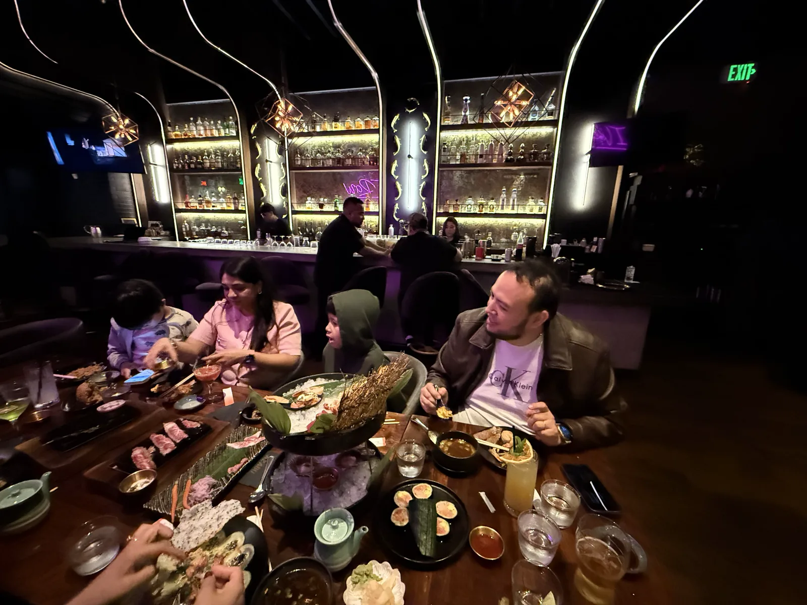 Carlos Salas and his family around a table full of sushi, Wagyu and a seafood tower, with Azabu's glowing back bar behind them